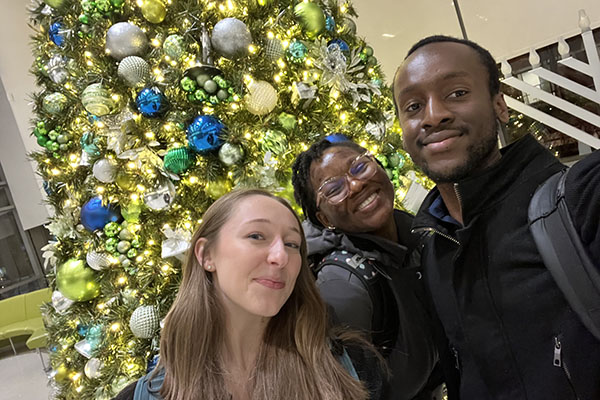 A festive interior view of the Johns Hopkins hospital atrium during Research Day, featuring a large, decorated holiday tree in the background with scientific posters and event signage in the foreground.