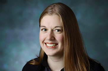 A professional headshot of Dr. Christina Miller, MD, an Associate Professor of Anesthesiology and Critical Care Medicine and Otolaryngology-Head and Neck Surgery. She is smiling warmly with a bright, engaged expression against a textured, professional blue studio background. She is wearing a black collared button-down shirt. The photograph has a high-fidelity, polished finish.