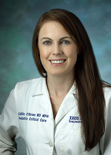 A professional headshot of Dr. Caitlin O'Brien, MD, an Assistant Professor of Anesthesiology and Critical Care Medicine. She is smiling warmly and wearing a clean white medical lab coat against a textured teal-blue studio background.